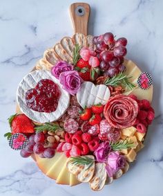 a platter filled with fruit and cheese on top of a marble countertop next to a cutting board