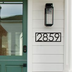 a green door with a house number sign on the side and a black mailbox