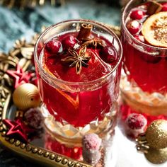 two glasses filled with red liquid and garnished with christmas decorations on a tray