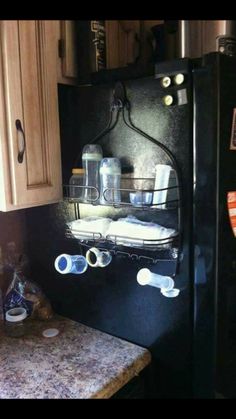 a black refrigerator freezer sitting inside of a kitchen next to a counter with cups on it