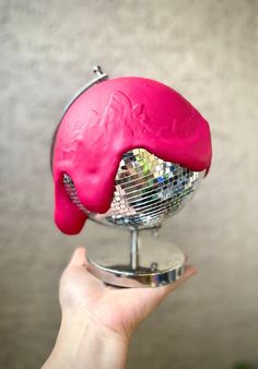 a person holding up a pink object in front of a mirror ball with its reflection on it