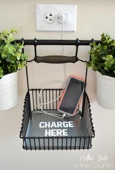 a cell phone charging in a wire basket with plants behind it and the text charge here