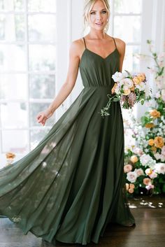 a woman in a long green dress standing next to a flower arrangement and smiling at the camera