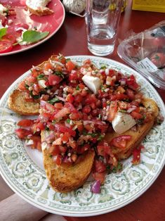 toasted bread topped with tomatoes and onions on a plate next to a glass of water