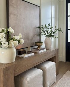 a wooden table topped with white vases filled with flowers next to a wall mounted art piece