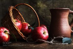 some apples are sitting next to a basket and jug on a table with twine