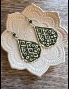 two green beaded earrings sitting on top of a white plate