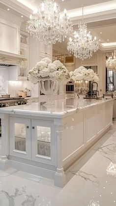 an elegant kitchen with chandelier and marble counter tops, white cabinetry, and flowers on the island