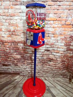 a red white and blue gummy machine on top of a wooden floor next to a brick wall