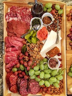 an assortment of meats and vegetables are displayed on a wooden tray with spoons