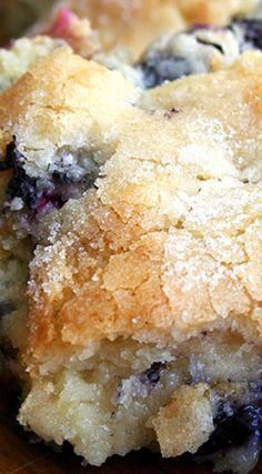 a close up of a blueberry cobbler on a wooden cutting board with a bite taken out