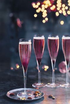 three glasses of wine sitting on top of a table next to each other with lights in the background