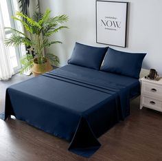 a bed with blue sheets and pillows in a room next to a potted plant