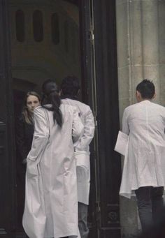 several people in white coats are standing at the door to a building with black doors