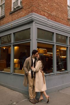 a man and woman are kissing in front of a storefront with people walking by