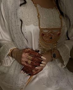 a woman wearing a white dress and holding her hands on her chest with gold jewelry