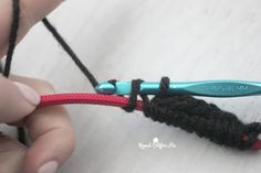 someone crocheting the end of a piece of yarn with a blue and red hook