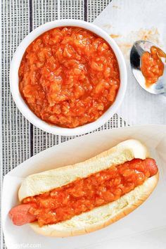 a hot dog in a bun with chili on it and a spoon next to it