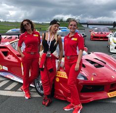 three women standing next to a red sports car