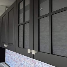 a kitchen with black cabinets and white counter tops in front of a red brick wall