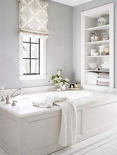 a white bath tub sitting under a window next to a shelf with towels on it