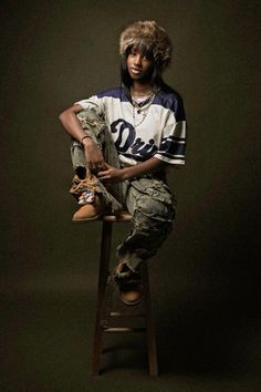 a young man sitting on top of a wooden stool wearing a hat and holding a skateboard