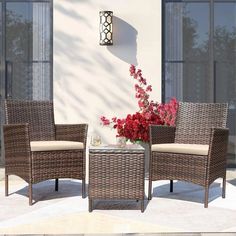 two wicker chairs and a table with flowers in front of a white building on a sunny day