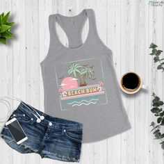 Beach Bum, Tropical Sunset and Palm Tree vintage style racerback workout or casual tank top. The model in the black tank top on the beach is 5'4'' 140lbs and is wearing a size L for a relaxed fit. Slim Fit Next Level Racerback tank-top (sizing chart in images) Material: 60% combed, ring-spun cotton, 40% polyester Extra light fabric (4 oz/yd² (135 g/m²)) Slim fit Runs slightly small since it is a slim fit. I suggest ordering one size up if you prefer a looser fit in your tank tops. Average Proces Summer Workout Tank Top With Graphic Print, Sleeveless Tank Top For Beach Season Sports, Sleeveless Tank Top For Beach Sports, Sleeveless Tank Top For Beach Workout, Sleeveless Workout Tank Top For Beach Season, Beach Racerback Top With Graphic Print, Racerback Graphic Print Top For Beach, Racerback Tops With Graphic Print For Beach, Graphic Print Racerback Tops For Beach