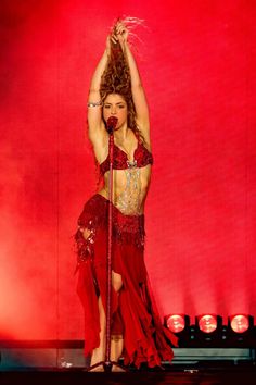 a woman in a red dress on stage with her arms up and hands behind her head