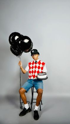 a man sitting on a chair holding two black balloons in his hand and wearing a checkered shirt