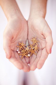 two hands holding starfish and pearls in their palms