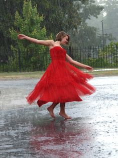 a woman in a red dress is dancing in the rain