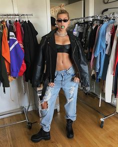 a woman standing in front of a rack of clothes and wearing black leather jacket with ripped jeans