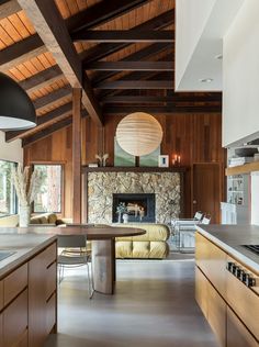 an open kitchen and living room area with wood paneling on the ceiling, stone fireplace in the center