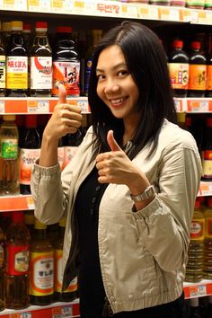 a woman is giving the thumbs up sign in front of shelves with various drinks and condiments