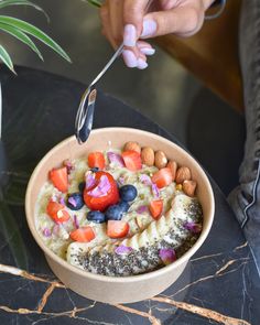 a bowl filled with fruit and nuts on top of a table next to a plant