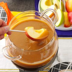 a person is dipping an apple into a glass bowl with caramel and apples in the background