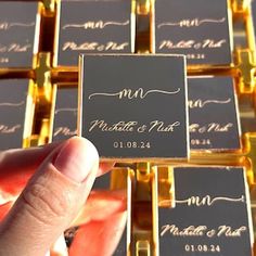 a person holding up some business cards in front of gold and black boxes with writing on them