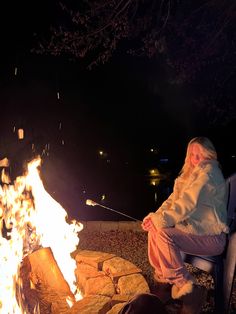 a woman sitting next to a campfire at night