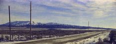 an empty road in the middle of nowhere with snow on the ground and mountains in the background