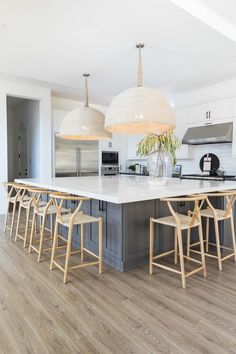 a large kitchen island with stools and lights hanging from it's ceiling above