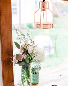 vases with flowers and greenery sit on a window sill in front of a light fixture