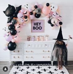 a room decorated for halloween with black and pink balloons, witch hats and bats on the wall