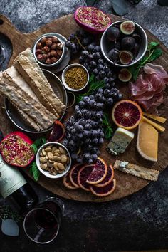 a wooden board topped with lots of different types of food next to bottles of wine