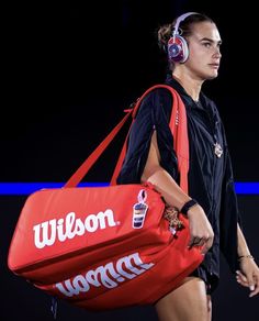 a woman in headphones carrying a red duffel bag on the runway at an event