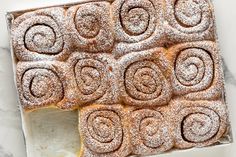 a pan filled with cinnamon rolls covered in powdered sugar on top of a marble counter