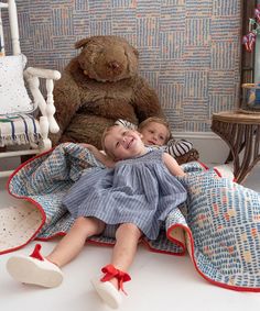 two children laying on the ground next to a large teddy bear and other toys in a room