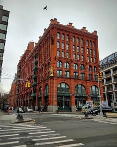 an old red brick building on the corner of a street with traffic lights and pedestrians