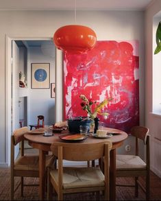 a dining room table and chairs with an orange painting on the wall in the background