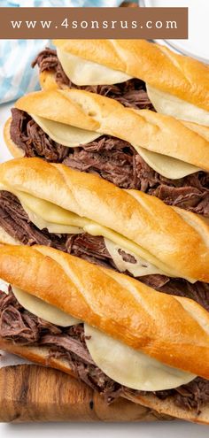 two roast beef sandwiches sitting on top of a wooden cutting board next to a blue and white towel